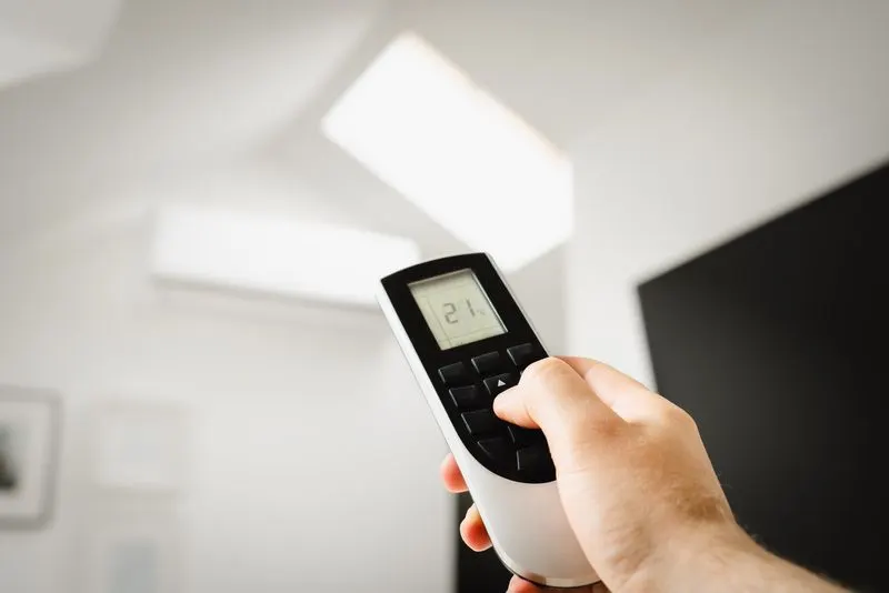 Hand pointing a remote control at a wall-mounted mini-split unit
