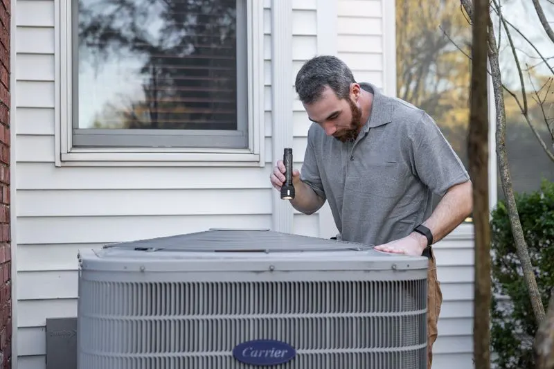 Technician shining a flashlight while inspecting an outdoor home air-conditioning unit