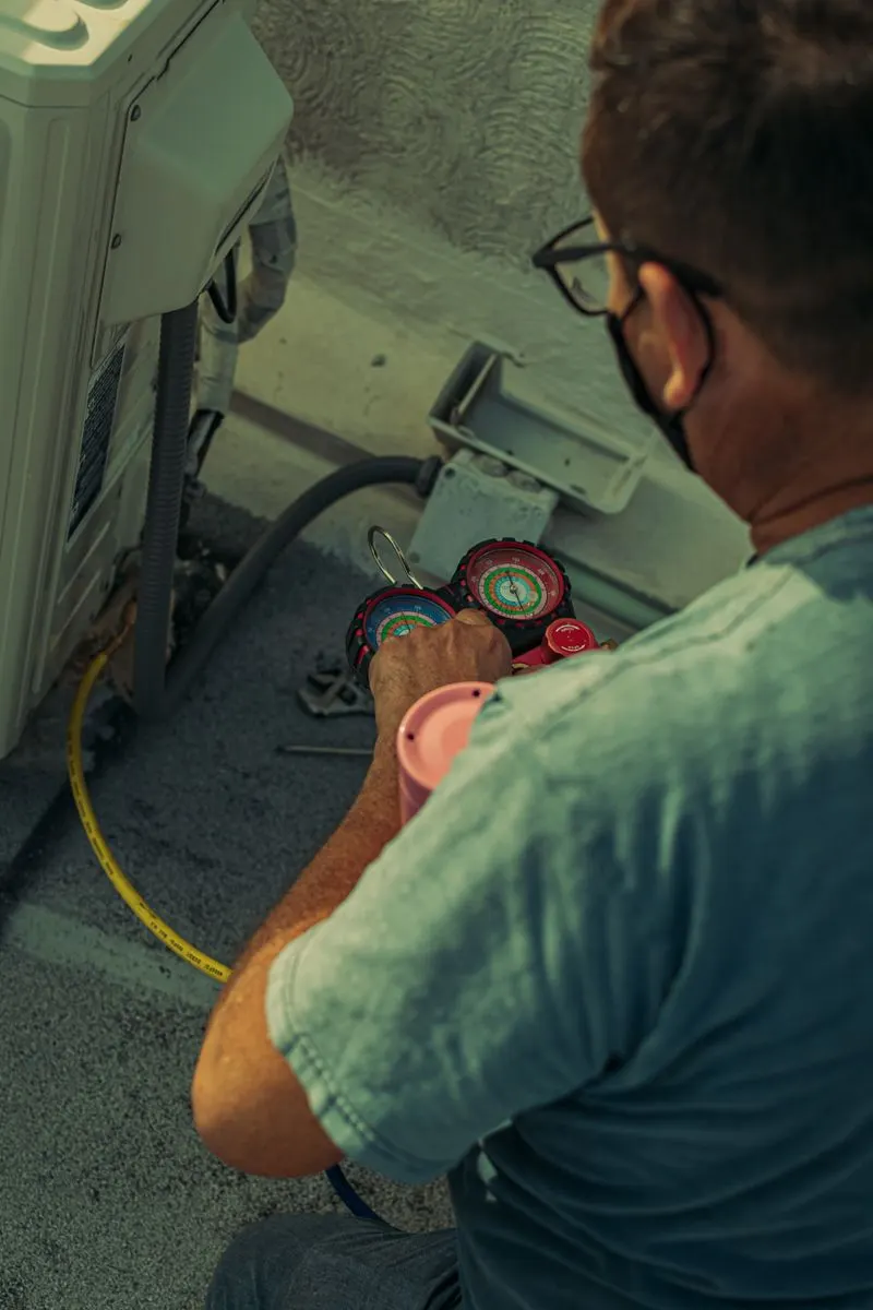 Technician using refrigerant gauges beside an outdoor mini-split condenser unit